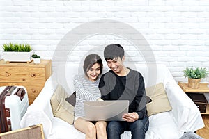 Young asian couple looking at laptop computer to search for travel plan, book hotel room, buy ticket or purchase travel insurance