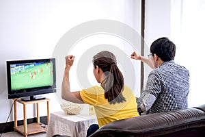 Young Asian couple love watching soccer match on tv and cheering