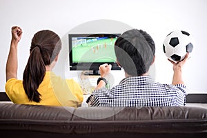 Young Asian couple love watching soccer match on tv and cheering
