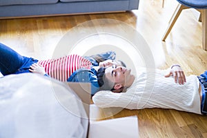 Young asian couple lying on the floor of new house arround cardboard boxes relaxing and smiling happy