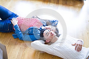 Young asian couple lying on the floor of new house arround cardboard boxes relaxing and smiling happy