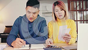 Young asian couple managing finances, reviewing their bank accounts using laptop computer and calculator at modern home.