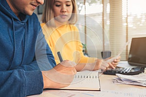 Young asian couple managing finances, reviewing their bank accounts using laptop computer and calculator at modern home.