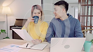 Young asian couple managing finances, reviewing their bank accounts using laptop computer and calculator at modern home.