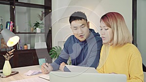 Young asian couple managing finances, reviewing their bank accounts using laptop computer and calculator at modern home.