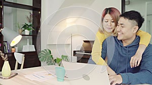 Young asian couple managing finances, reviewing their bank accounts using laptop computer and calculator at modern home.