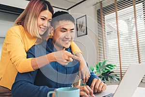 Young asian couple managing finances, reviewing their bank accounts using laptop computer and calculator at modern home.