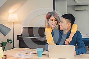 Young asian couple managing finances, reviewing their bank accounts using laptop computer and calculator at modern home. Woman and