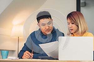 Young asian couple managing finances, reviewing their bank accounts using laptop computer and calculator at modern home. Woman and