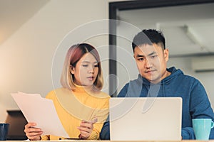 Young asian couple managing finances, reviewing their bank accounts using laptop computer and calculator at modern home. Woman and