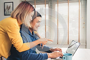 Young asian couple managing finances, reviewing their bank accounts using laptop computer and calculator at modern home. Woman and