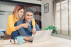 Young asian couple managing finances, reviewing their bank accounts using laptop computer and calculator at modern home. Woman and