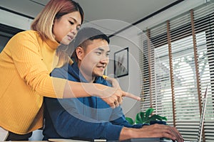 Young asian couple managing finances, reviewing their bank accounts using laptop computer and calculator at modern home. Woman and