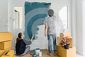 Young asian couple painting interior wall with paint roller in n
