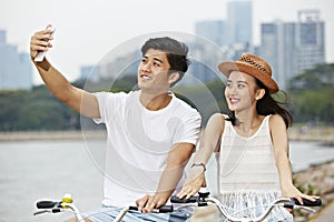 Young asian couple riding bike and taking a selfie