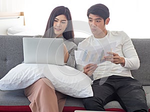 Young asian couple sit on a coach in bedroom discuss their works using notebook computer. Online work from home
