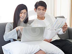 Young asian couple sit on coach in living room enjoy working from home using laptop and internet connection. Modern lifestyle