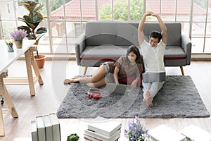 Young Asian couple sitting on floor and using laptops together at home, working from home concept