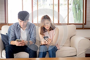 Young asian couple sitting on sofa with problem about relationship because addicts social network media together