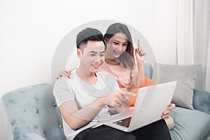Young asian couple surfing on internet and shopping with laptop. Modern white apartment in background