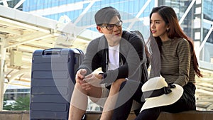 Young Asian couple travelers  and luggage sitting and talking  in city . Lover tourists travel in vacation outdoors