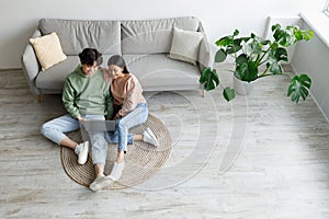 Young Asian couple using laptop, surfing internet or watching movie online, sitting on floor in living room, top view