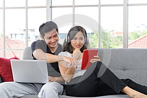 Young asian couple wear casual clothing relax sitting on cozy couch in living room. Man working on laptop. Woman with headphones