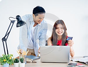 Young Asian couple, woman holding credit card and man happy after using laptop computer together.