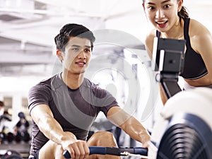 Young asian couple working out using rowing machine