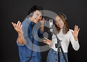 Young asian couples with headphones sing in chorus with microphone and pop filter on tripod stand. Musicians producing music in