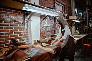 Young asian craftswoman working at desk in leather fabric