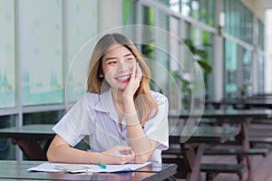 Young Asian cute girl student is using smart phone to search information for a study report she smiled happily while sitting in