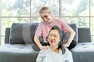 Young Asian daughter massages shoulder, relieves pain of elderly Asian mother while sitting on the sofa at home, Family concept.