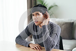 Young Asian deaf disabled man having hearing problems holds his hand over the ear, listens carefully, hard of hearing