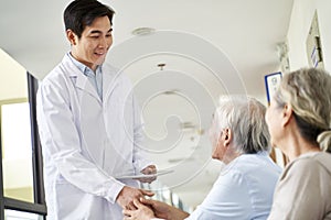 Young asian doctor shaking hands with senior patient