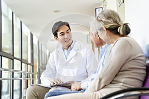 Young asian doctor talking to senior couple patients in hospital hallway photo