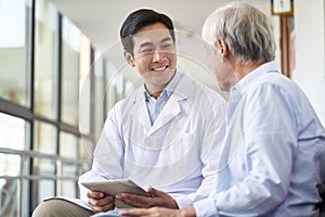 Young asian doctor talking to senior man in hospital hallway