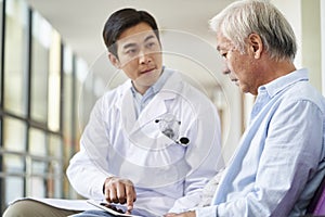 Young asian doctor talking to senior man in hospital hallway