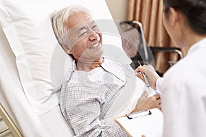 Young asian doctor talking to senior patient at bedside in hosptial ward