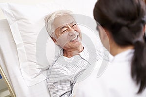 Young asian doctor talking to senior patient at bedside in hosptial ward