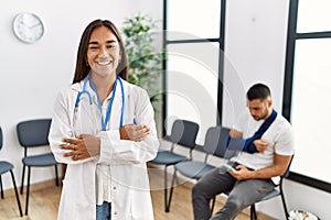 Young asian doctor woman at waiting room with a man with a broken arm happy face smiling with crossed arms looking at the camera