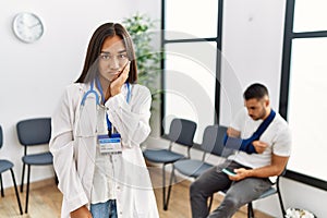 Young asian doctor woman at waiting room with a man with a broken arm thinking looking tired and bored with depression problems
