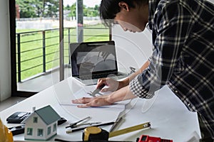 Young Asian engineer drawing construction project plans on plan paper on table in office