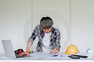 Young Asian engineer drawing construction project plans on plan paper on table in office