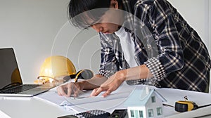 Young Asian engineer drawing construction project plans on plan paper on table in office