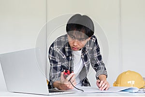 Young Asian engineer drawing construction project plans on plan paper on table in office