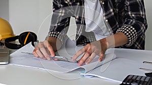 Young Asian engineer drawing construction project plans on plan paper on table in office