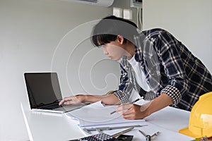 Young Asian engineer drawing construction project plans on plan paper on table in office