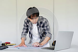 Young Asian engineer drawing construction project plans on plan paper on table in office