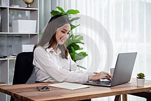 Young asian enthusiastic businesswoman at modern office desk with laptop.